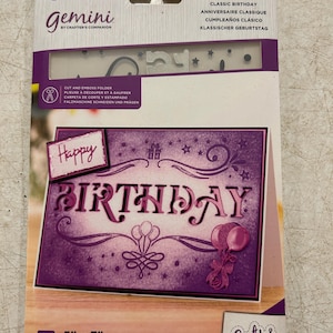 May include: A purple and white Gemini cut and emboss folder for making birthday cards. The design includes the word "BIRTHDAY" with balloons and stars. The package is 5" x 7" (12.7cm x 17.7cm).