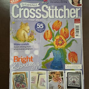 May include: A magazine cover for CrossStitcher, featuring a stitched floral design in a blue vase. The cover includes text such as "Bright & breezy" and "55 inspirational designs". The magazine is a "Best Seller".