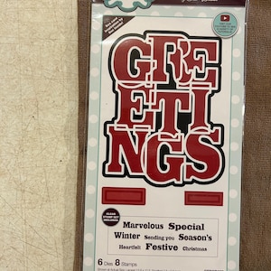 May include: A craft die and stamp set in a clear plastic package. The set includes steel dies and clear stamps with the word "GREETINGS" in red and black. Additional text includes "Marvelous Special Winter Season's Heartfelt Festive Christmas".