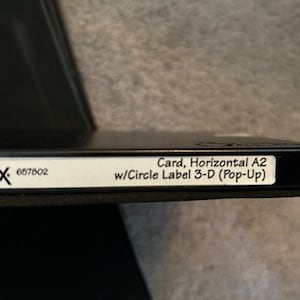 May include: A black Sizzix die cutting machine with a white label that reads "Card, Horizontal A2 w/Circle Label 3-D (Pop-Up)" and the number 657802.