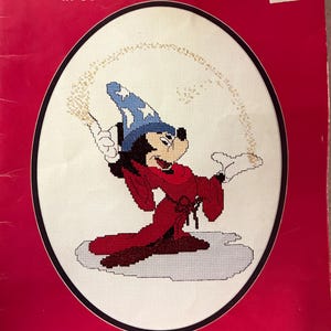 May include: A counted cross stitch pattern featuring Mickey Mouse as a sorcerer, with a red robe and blue hat, casting a spell with a magic wand. The pattern is from Walt Disney Characters in Counted Cross Stitch, Book 5070, designed by Gloria & Pat for Paragon Needlecraft.