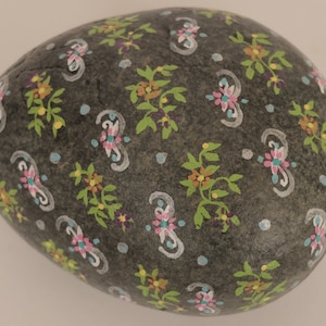 May include: A gray stone egg painted with a floral pattern in shades of pink, blue, green, orange, and white.