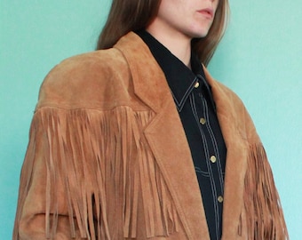 May include: A brown suede jacket with fringe detailing on the shoulders and sleeves. The jacket has a button closure and a single button pocket on the left side.