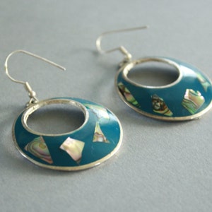 May include: A pair of silver hoop earrings with a turquoise blue enamel finish. The earrings are decorated with iridescent abalone shell pieces.