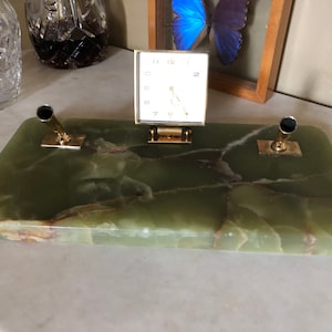 May include: A green marble desk set with two pen holders and a small clock. The clock has a white face with black numbers and hands.