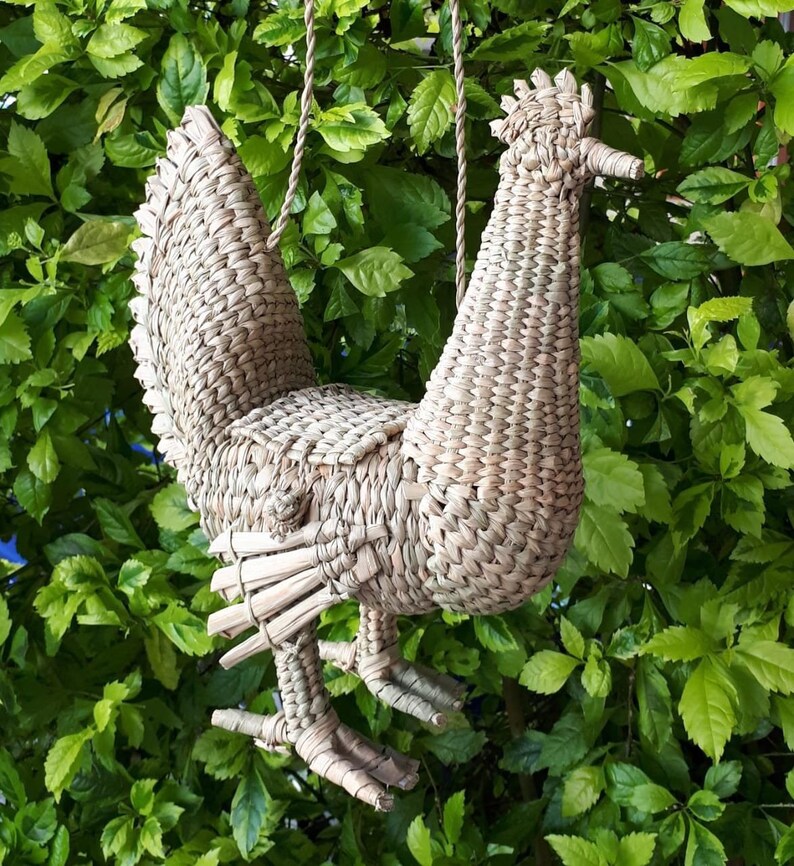 May include: A woven straw bird-shaped handbag with a long strap. The bird has a long neck and a tail that is fanned out. The handbag is a light brown colour.