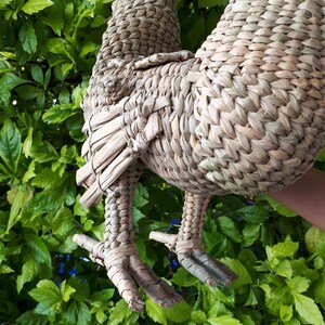 May include: A woven straw rooster figurine with detailed legs and feet. The rooster is light brown and has a natural, rustic look.