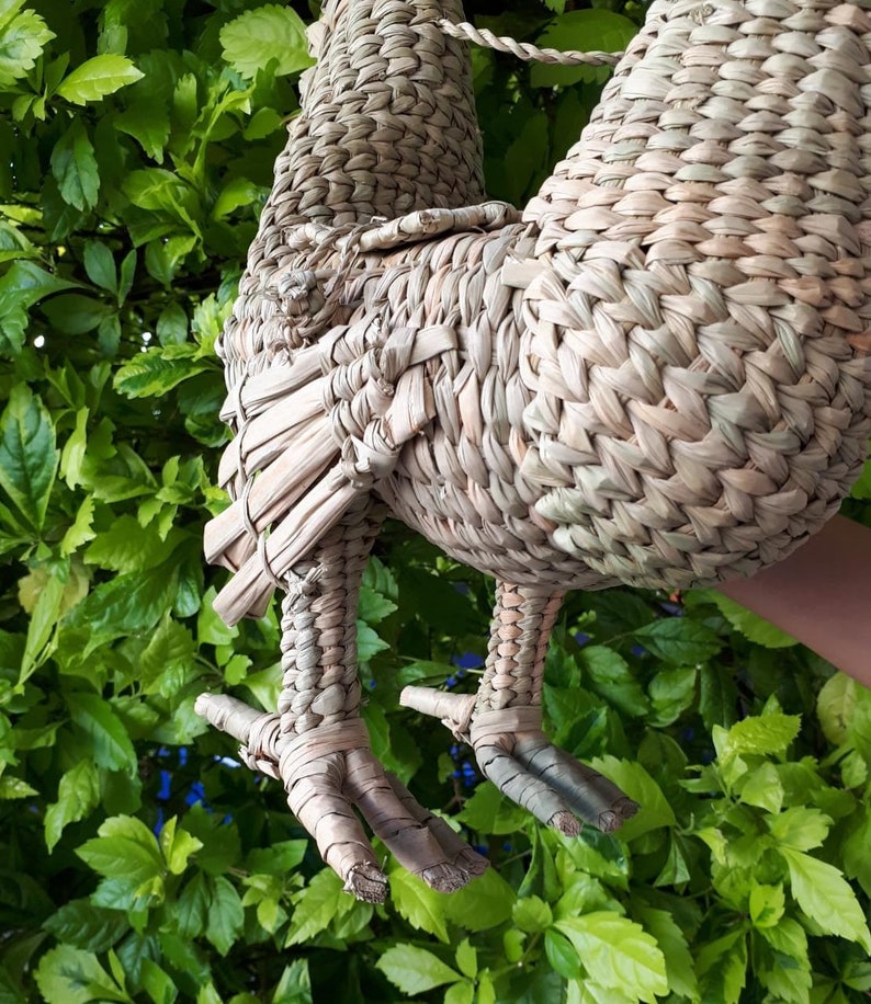 May include: A woven straw rooster figurine with detailed legs and feet. The rooster is light brown and has a natural, rustic look.
