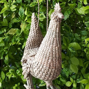 May include: A woven straw chicken-shaped hanging decoration with a brown rope. The chicken is hanging from a tree branch.