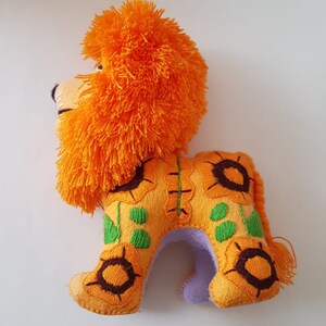 Puede incluir: Le&oacute;n de fieltro naranja y amarillo con girasoles bordados. El le&oacute;n mide 25,4 cm de largo, 17,8 cm de alto y 10,2 cm de ancho.