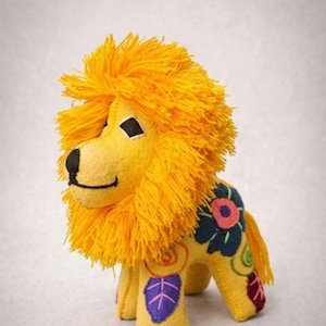 May include: A yellow plush lion toy featuring a thick, bright yellow yarn mane, a black stitched nose and mouth, and diamond-shaped eyes. The body is decorated with colorful embroidered floral and leaf patterns in blue, pink, purple, and green.