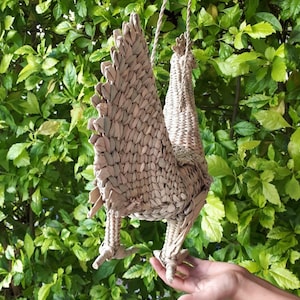 May include: A woven wicker rooster figurine with a long tail, hanging from a rope. The rooster is light brown in colour and has a detailed design.