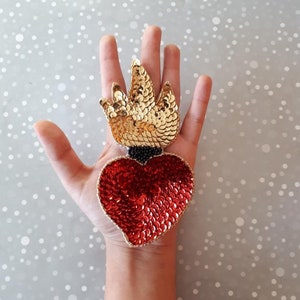 May include: A red heart with gold sequins and a gold flame design. The heart is surrounded by black sequins.