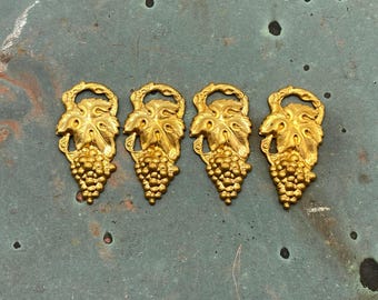 Könnte beinhalten: Vier goldfarbene dekorative Traubencluster-Ornamente. Jedes Ornament zeigt eine Traube und detaillierte Blätter. Die Ornamente sind in einer Reihe auf einer gesprenkelten grün-grauen Oberfläche angeordnet.