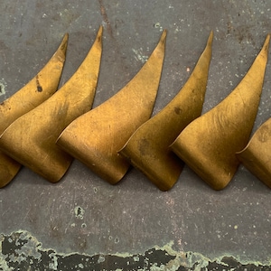 May include: Six gold-colored metal decorative pieces shaped like a sharp, pointed leaf. The pieces are arranged in a row, with the points facing the same direction.