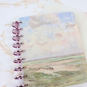 Puede incluir: Un diario con espiral con un dise&ntilde;o de paisaje en acuarela que presenta un campo y un cielo. La portada tiene el texto "This is my comfort in my affliction..." y "Psalm 119:50" en escritura blanca. El diario tiene anillos de oro rosa.