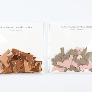 May include: Two clear plastic bags filled with photo corners. One bag contains copper-colored corners, and the other contains pink and gray corners. The text "PERSONALIZE MY PLANNER" is printed on the top of each bag.