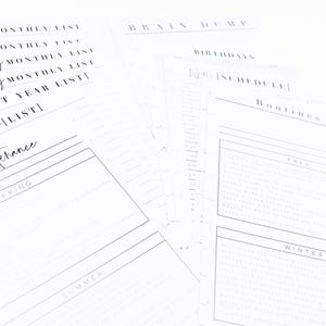 May include: A collection of white planner pages with handwritten text. The pages include lists for months, a next year list, and sections for maintenance, spring, summer, fall, and winter. Other pages include a brain dump, birthdays, and a weekly schedule.