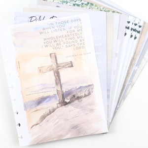 May include: A stack of printed pages with a watercolor illustration of a cross on a hill. The pages have text from Jeremiah 29:13. The pages are fanned out against a white background.