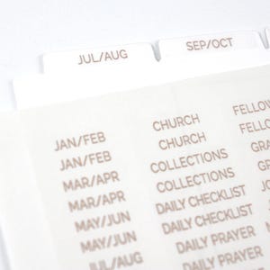 May include: Close-up of white planner dividers and stickers. The dividers are labeled with months like "JUL/AUG" and "SEP/OCT." The stickers list categories such as "CHURCH," "FELLOWSHIP," and "DAILY CHECKLIST." Ideal for organizing a planner.