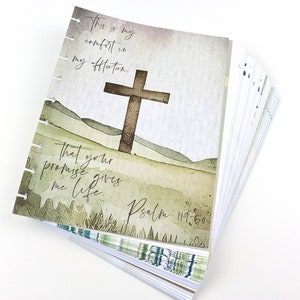 May include: A stack of watercolor-style journal pages with a cross and inspirational text. The pages feature a brown cross against a backdrop of green hills and the words "This is my comfort in my affliction" and "That your promise gives me life."
