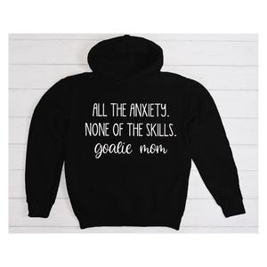 Może przedstawiać: Czarna bluza z kapturem z białym napisem "All the anxiety. None of the skills. goalie mom."