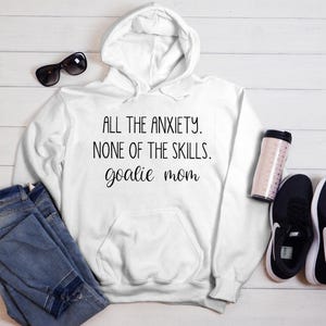 Może przedstawiać: Biała bluza z kapturem z nadrukiem "All the anxiety. None of the skills. goalie mom" z przodu.