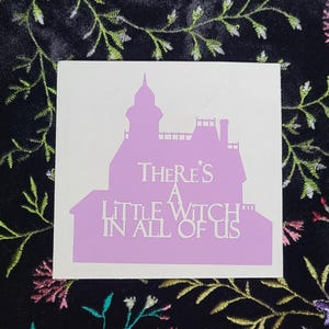 May include: A pink silhouette of a house with the text "There's a little witch in all of us" printed in white.