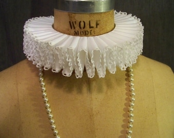 May include: A white, ruffled Elizabethan collar with a delicate lace trim, displayed on a vintage mannequin. A strand of faux pearls hangs in front of the collar. The mannequin's neck has the text "WOLF MODEL".