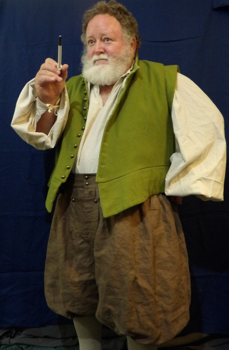Op de afbeelding: Een persoon in historische kleding, met een groen vest met gouden knopen over een wit overhemd met pofmouwen. Hij draagt ook bruine, bolle broeken en houdt een pen vast. De outfit doet denken aan de Renaissance.