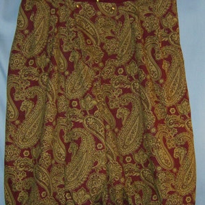 Op de afbeelding: Bordeaux rok met een gouden paisley patroon. De rok heeft een geplooide, ballonachtige vorm aan de onderkant en hangt aan een witte hanger. Gouden knopen sieren de tailleband.