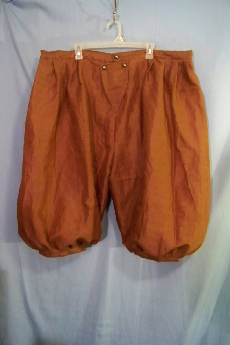 Op de afbeelding: Roestkleurige, knielange pofbroek met een hoge taille en gerimpelde manchetten. De shorts hebben een knoopsluiting en hangen aan een witte plastic hanger. De stof lijkt een lichtgewicht materiaal te zijn.