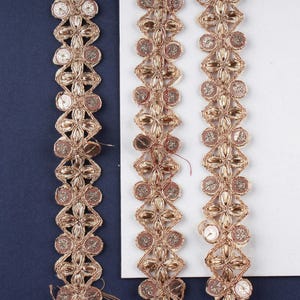 Puede incluir: Tres tiras de ribete dorado y marrón con lentejuelas y un diseño floral.