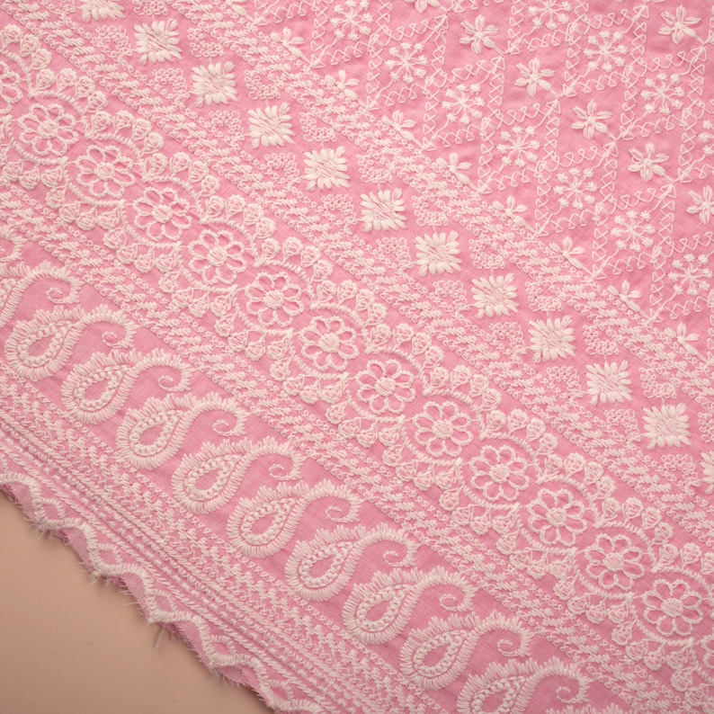 May include: Pink fabric with white embroidery in a paisley pattern.