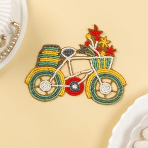 Puede incluir: Una bicicleta de cuentas con una cesta de flores. La bicicleta está hecha de cuentas verdes, amarillas, rojas y blancas. Las flores son rojas, amarillas y verdes.