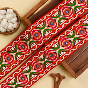 May include: Red, green, white, and blue embroidered trim with a repeating pattern of circles and swirls. The trim has a shiny, metallic finish.
