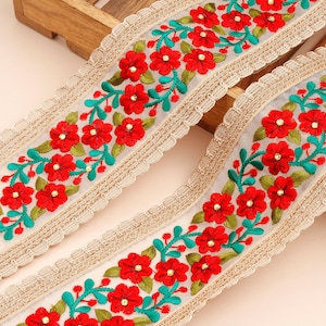 May include: Red and green floral embroidered trim with a scalloped edge. The trim is on a white background with a gold thread running through it.