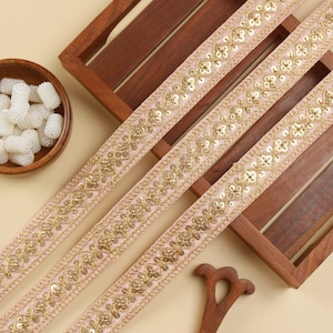 Peut inclure: Trois pièces de galon rose et or avec un motif géométrique et des paillettes.