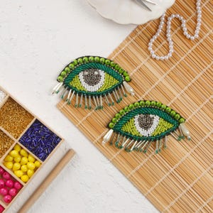 May include: Two green and white beaded eye patches with fringe. The eye patches are on a woven bamboo mat.