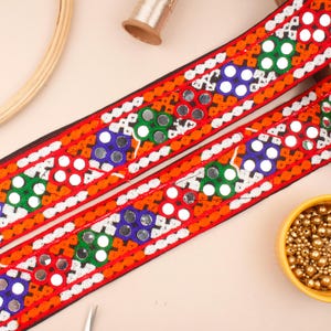 May include: Red, orange, green and blue embroidered trim with round, mirrored embellishments. The trim is on a black background.
