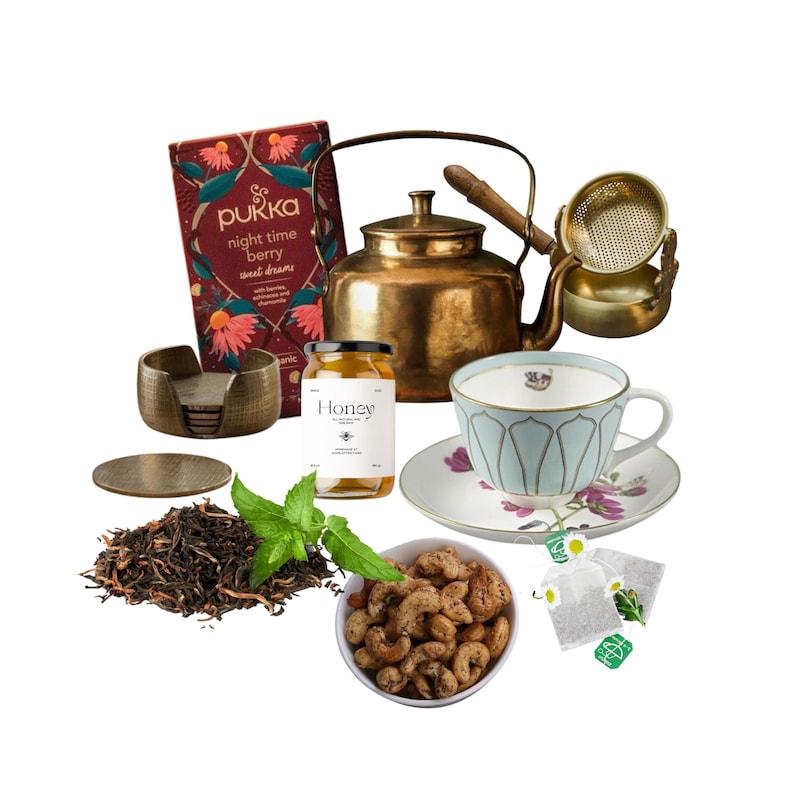 May include: A tea time set with a copper kettle, a teacup and saucer, a jar of honey, a box of Pukka Night Time Berry tea, a small bowl of cashews, and two tea bags.