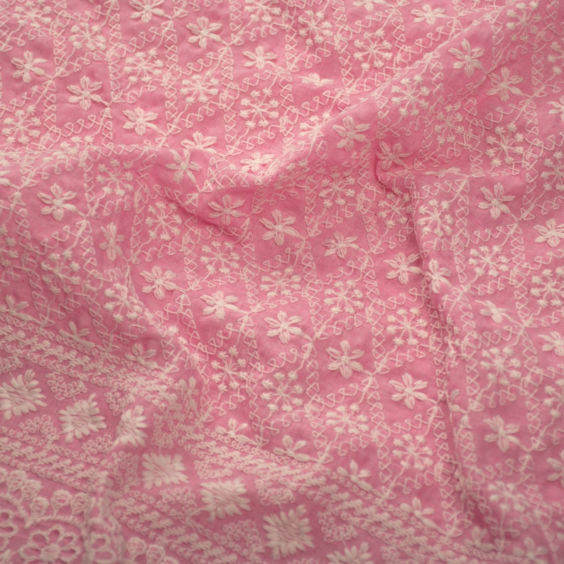 May include: Pink fabric with white embroidered floral pattern. The fabric is soft and delicate, with a subtle sheen.