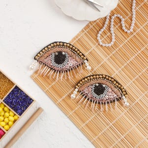 May include: Two beaded eye patches with pink, brown and black beads. The eye patches are on a woven bamboo mat.