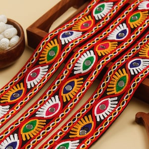 Puede incluir: Tres filas de ribete de tela negra con diseños de ojos bordados de colores y detalles de espejo. El ribete es rojo, amarillo, verde, azul y blanco.