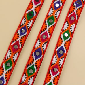May include: Three red, white, blue, green, and orange trim ribbons with mirrored accents. The ribbons have a repeating pattern of embroidered flowers and geometric shapes.