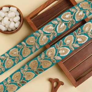 Könnte beinhalten: Tealblauer Stoffbesatz mit goldenen Blatt- und Pailletten-Stickereien. Der Besatz zeigt ein sich wiederholendes Muster aus Blättern und Blüten.