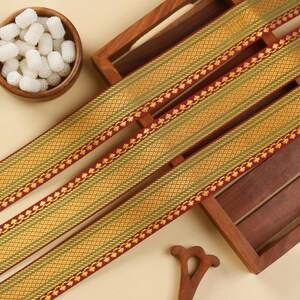 May include: Three pieces of maroon, gold and green trim with a diamond pattern and leaf accents. The trim is displayed on a wooden surface.