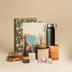 May include: A gift set with a floral patterned box, a green water bottle, a candle in a glass jar with a gold lid, a small blue notebook, a bar of soap, a small bottle of liquid, and a tube of lotion.