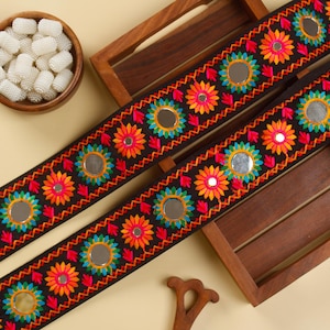 May include: Two black fabric trims with colourful embroidered flowers and round mirror accents.