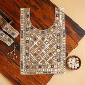 May include: A decorative textile piece with a scoop neckline, embellished with sequins and floral embroidery in gold, pink, blue, and green. The design features a diamond pattern. Includes a matching ribbon and small scissors.